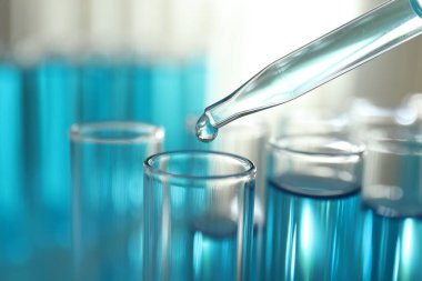 Işık arkaplanındaki test tüplerine sıvı damlatılıyor.