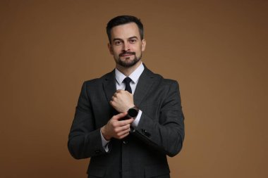 Kahverengi arka planda şık saati olan klasik takım elbiseli kendine güvenen bir adam.