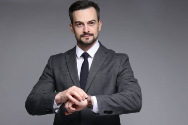 Klasik takım elbiseli kendine güvenen adam gri arkaplanı kontrol ediyor.