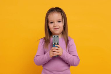 Turuncu arka planda mikrofonu olan tatlı bir kız.