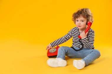 Turuncu arka planda telefonu olan sevimli küçük bir çocuk, mesaj için yeri var.