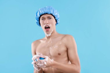 Duş bonesi ve açık mavi arka planda ağ süngeri olan bir adam.