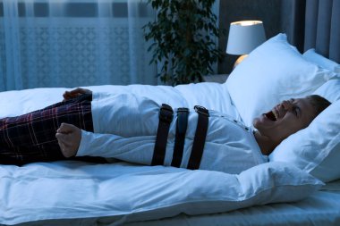 Uyurgezer bir adam yatakta çığlık atıyor.