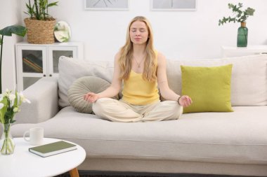 Feng shui. Evdeki kanepede meditasyon yapan genç bir kadın.
