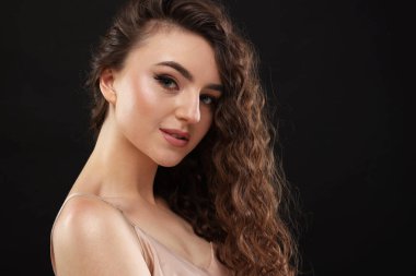 Siyah arka planda uzun kıvırcık saçlı güzel bir genç kadın.