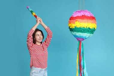 Mutlu kadın açık mavi arka planda renkli pinataya vuruyor.