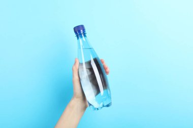 Açık mavi arka planda plastik su şişesi tutan kadın, yakın plan.