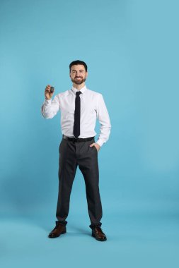 Açık mavi arka planda araba anahtarı olan neşeli bir satıcı.