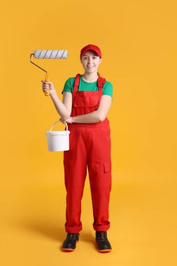 Turuncu arka planda bir kova boyası olan profesyonel bir ressam.