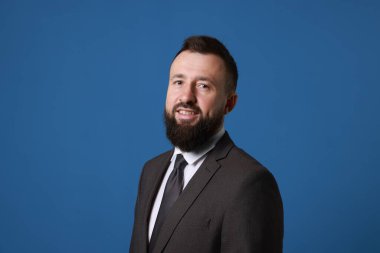 Mavi arka planda takım elbiseli yakışıklı sakallı adam.