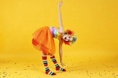 Palyaço gibi giyinmiş tatlı bir kız ve sarı arka planda konfeti. Sürpriz parti.