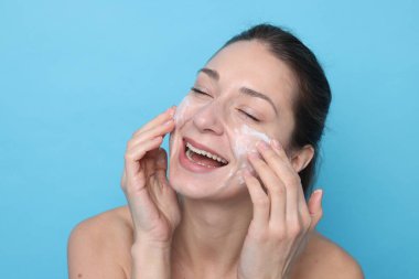 Spa günü. Yüzüne açık mavi arka planda maske takan mutlu kadın.