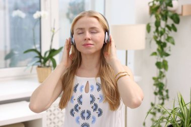 Feng shui. Kulaklıklı genç bir kadın evdeki çiçeklerin yanında müzik dinliyor.