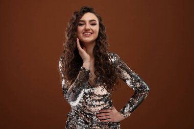 Kahverengi arka planda uzun kıvırcık saçlı, pullu elbiseli güzel bir kadın.