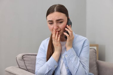 Stresli kadın, evdeki koltukta ruh sağlığı için yardım hattını arıyor.