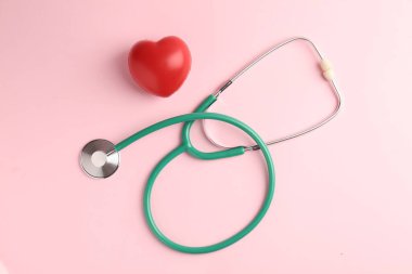 Kardiyoloji. Stetoskop ve soluk pembe arka planda kırmızı dekoratif kalp düz yatıyordu.
