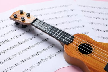 Pembe arka planda Ukulele ve müzik sayfaları, yakın plan