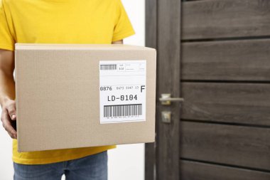 Kapıya yakın bir yerde nakliye etiketli paket taşıyan bir adam var. Yakın plan. Metin için boşluk