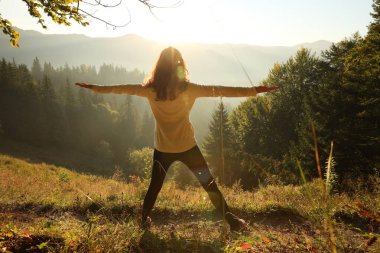 Gün doğumunda dağlarda yoga yapan bir kadın.