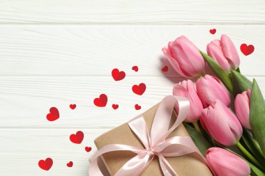 Güzel pembe laleler, hediye kutusu ve beyaz ahşap arka planda kırmızı kağıt kalpler.