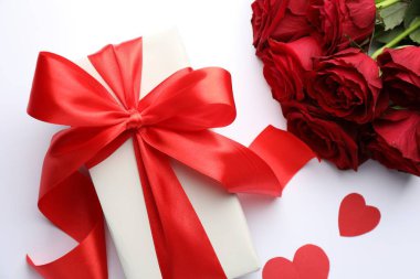 Kırmızı fiyonklu hediye kutusu, beyaz arka planda güzel güller ve kağıt kalpler, düz uzanmış