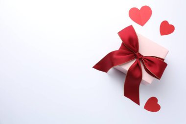 Kırmızı fiyonklu hediye kutusu ve beyaz arka planda kağıt kalpler, düz yatıyordu. Metin için boşluk