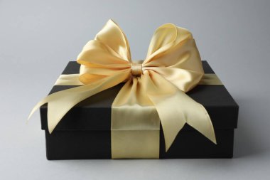 Gri arka planda altın fiyonklu hediye kutusu, yakın plan.