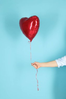 Açık mavi arka planda kırmızı kalp şeklinde balonu olan adam, yakın plan. Sevgililer Günün kutlu olsun.