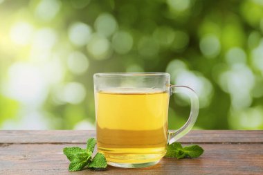 Cam fincanda aromatik nane çayı ve açık havada ahşap masada taze yapraklar.
