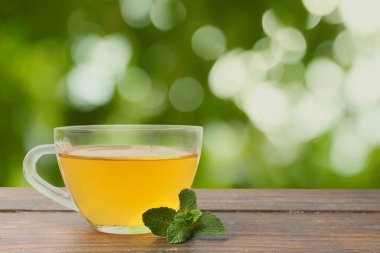 Cam fincanda aromatik nane çayı ve açık havada ahşap masada taze yapraklar. Metin için boşluk