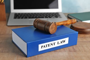 Ehliyet. Patent hukuku kitabı, yargıç tokmağı ve dizüstü bilgisayarı ahşap masada, yakın plan.
