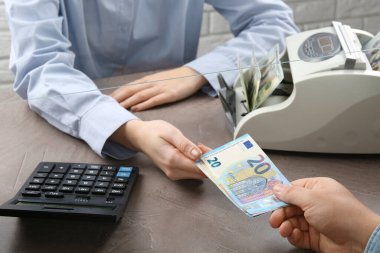 Müşteri para bozdurma masasındaki kasiyere avro banknotları veriyor, yakın plan