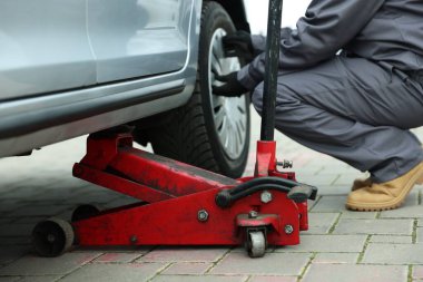 Makas kriko ile kaldırılan araba. Otomatik tamirci dışarıdaki tekerleği değiştiriyor, yakın plan.