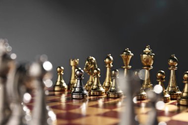 Satranç tahtasındaki altın satranç taşlarının önünde gri arka plana karşı gümüş piyon, yakın plan. Rekabet konsepti