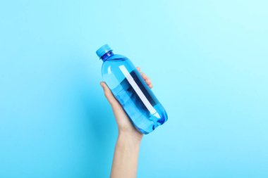 Açık mavi arka planda plastik su şişesi tutan kadın, yakın plan.