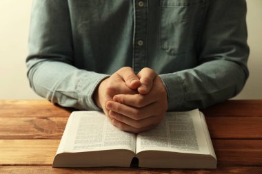 Kutsal kitabı olan bir adam ahşap masada dua ediyor, yakın plan.