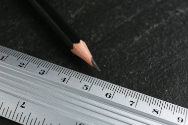 Metal cetvel ve kalem siyah masada, yakın plan.