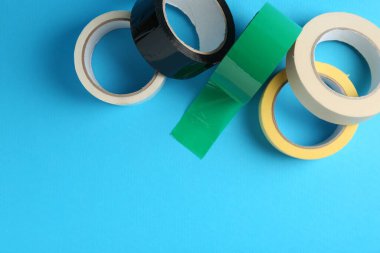 Açık mavi arka planda farklı yapışkan bantların ruloları, düz. Metin için boşluk