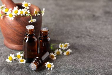 Gri masada gerekli yağ şişeleri ve papatya çiçekleri. Metin için boşluk