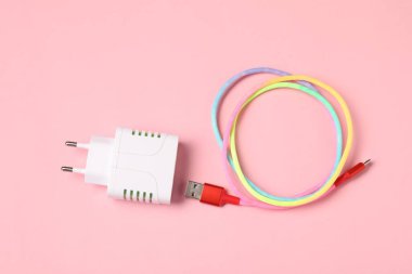 USB güç adaptörü ve soluk pembe arka planda şarj kablosu, düz yatıyordu