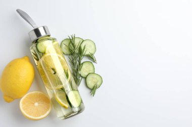 Şişe içinde limon suyu, biberiye, taze meyve ve beyaz arka planda salatalık dilimleri, düz yatak. Metin için boşluk