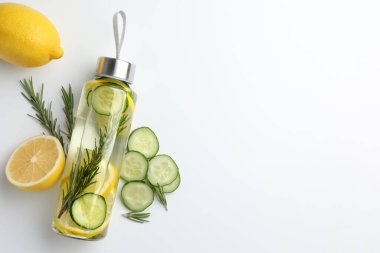 Şişe içinde limon suyu, biberiye, taze meyve ve beyaz arka planda salatalık dilimleri, düz yatak. Metin için boşluk