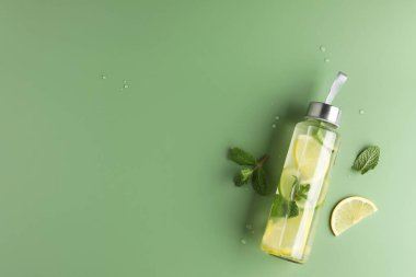 Şişe içinde naneli limon suyu, taze yapraklar ve yeşil arka planda bir dilim meyve. Metin için boşluk