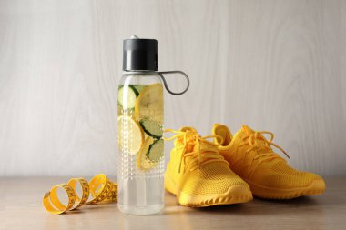 Şişe içinde salatalıklı limon suyu, tahta yüzey üzerinde şerit ve spor ayakkabıları.
