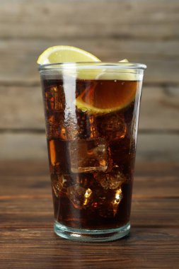 Ahşap masada limon dilimleri ile buzlu kola tazeleniyor, yakın plan.
