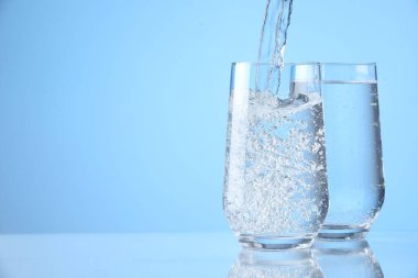 Açık mavi arkaplandaki bardaklara taze soda dökülüyor, yakın plan. Metin için boşluk