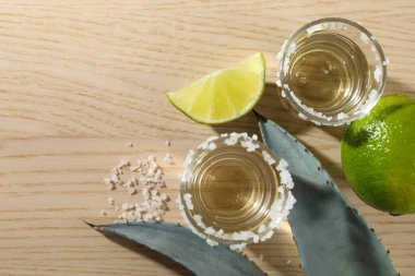 Tuzlu, limonlu ve agave yapraklı tekila kadehleri ahşap masada, düz yerde. Metin için boşluk