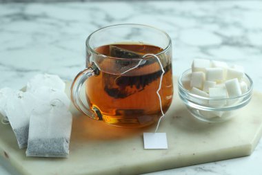 Cam bardakta çay poşeti, sıcak içecek ve şeker küpleri açık mermer masada, yakın plan.