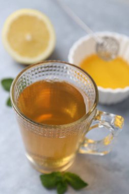 Cam bardakta aromatik nane çayı, taze yapraklar, açık gri masada bal ve limon, yakın plan.