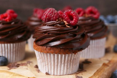 Çikolata kremalı ve ahududulu lezzetli kekler ahşap tahtada, yakın plan.